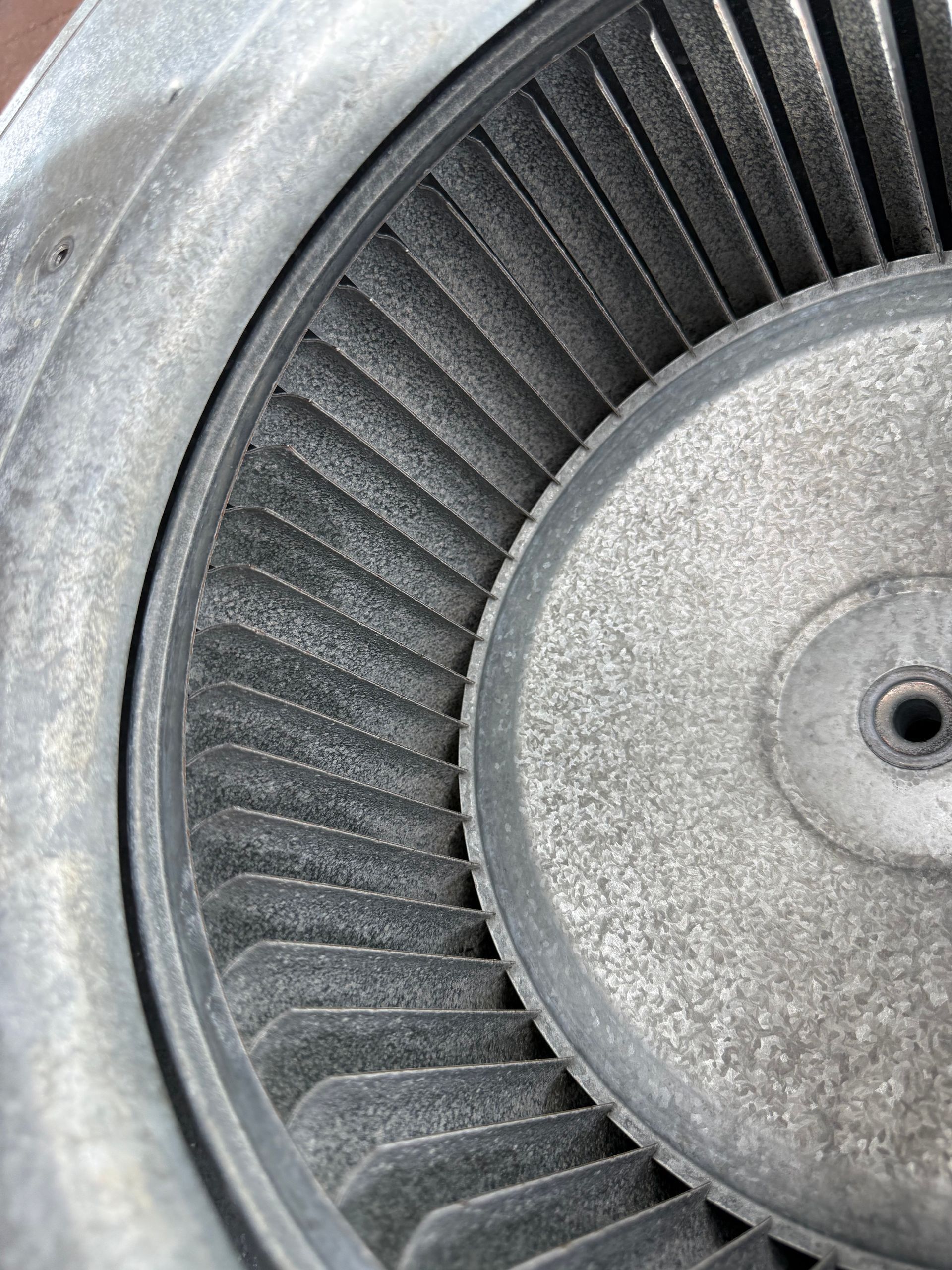 A close-up, top-down view of a circular, metal HVAC blower wheel covered in a thick layer of grey dust and debris.