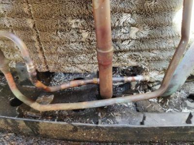 Copper refrigerant lines with soldered joints emerge from a dirty air conditioner coil.