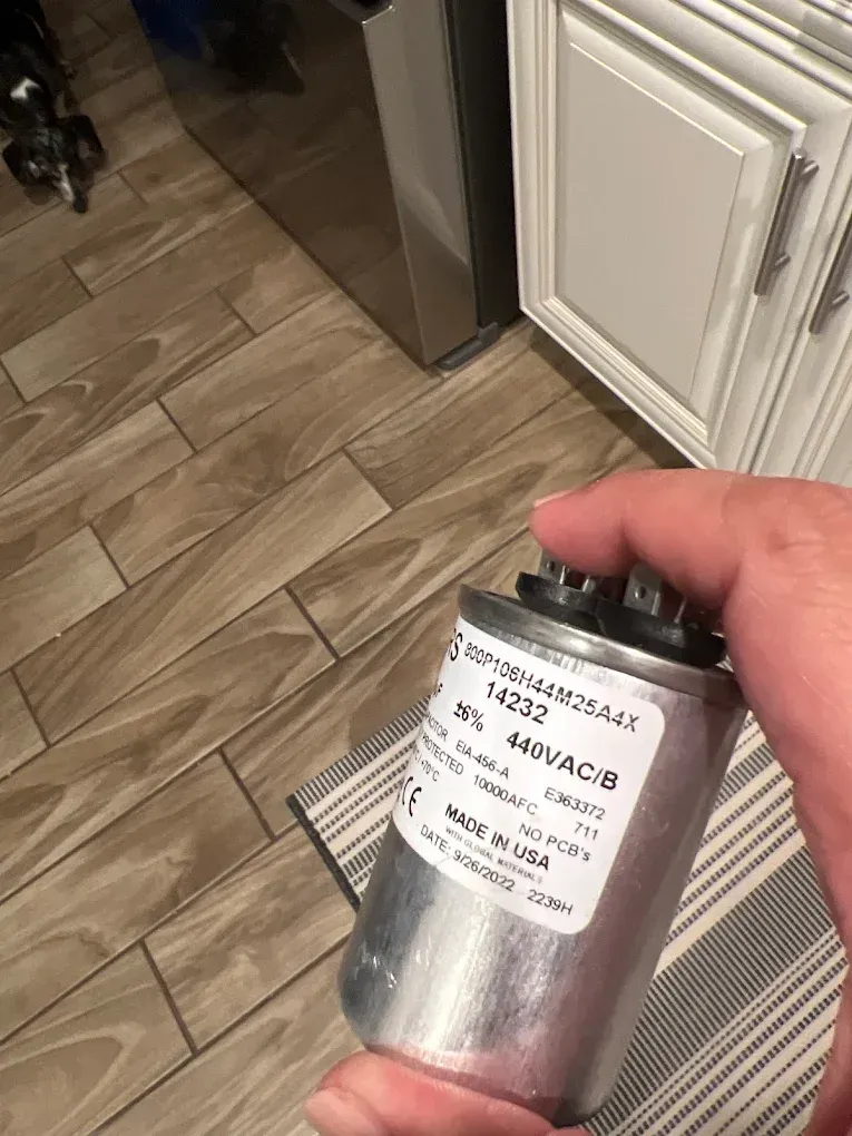 Person holding a silver capacitor with a label in a kitchen.