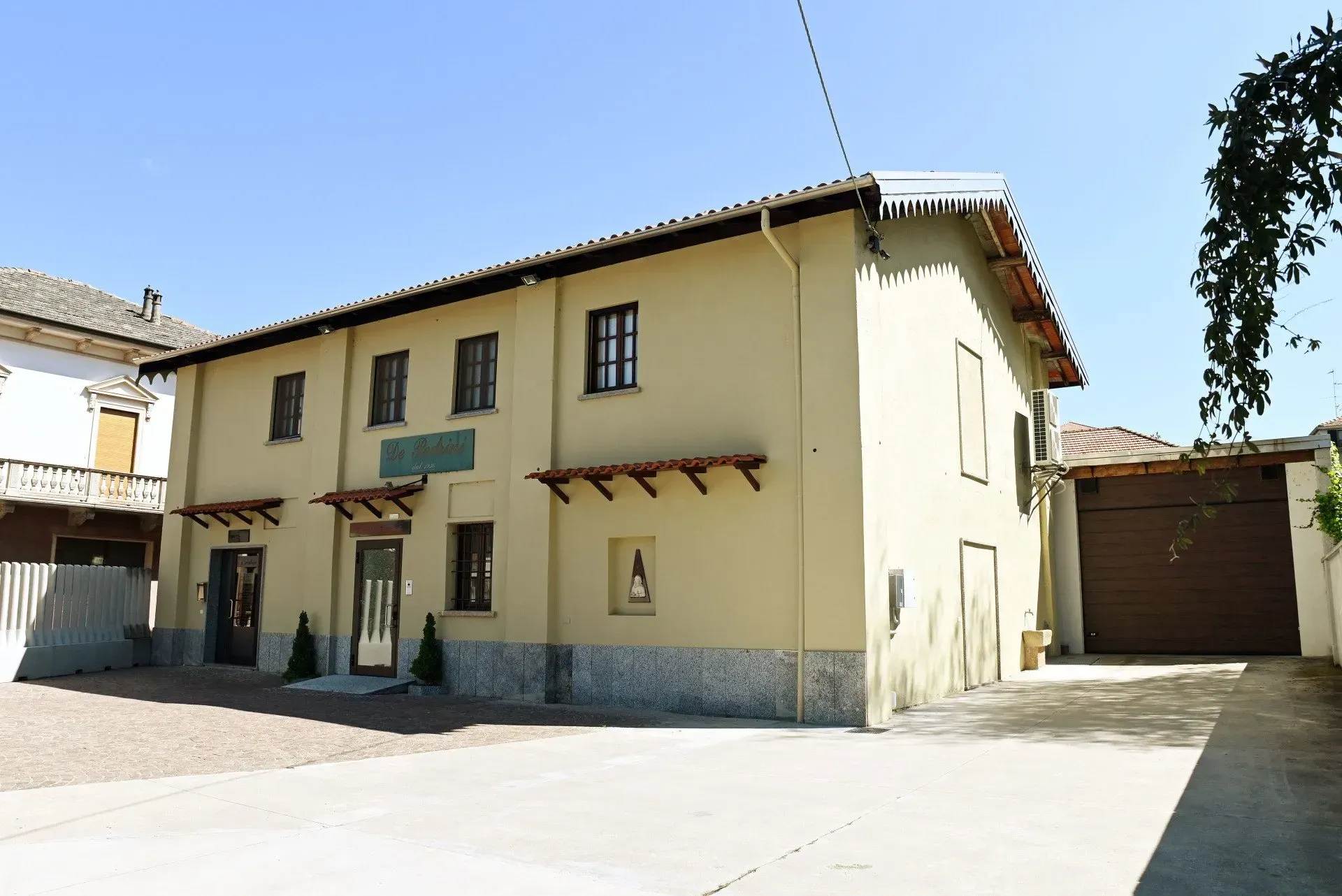 Edificio a due piani con facciata beige, tetto marrone e porta del garage laterale.