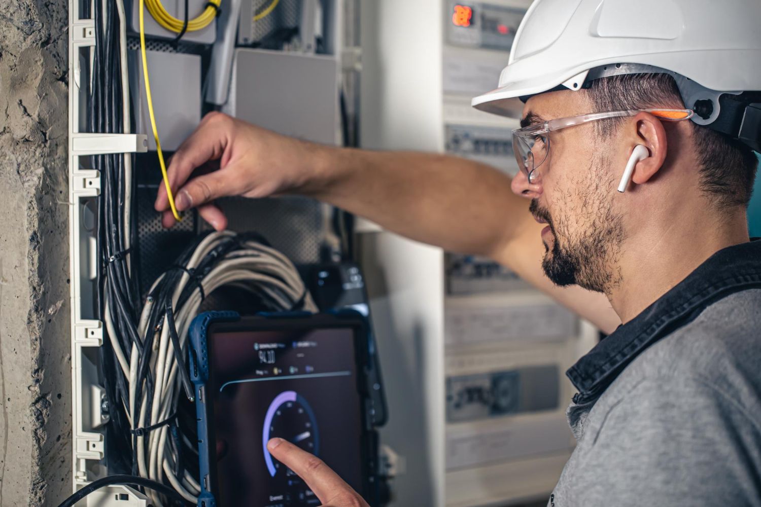 A man wearing a hard hat and headphones is working on an electrical box.