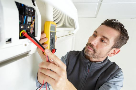 a man is working on an air conditioner with a multimeter .