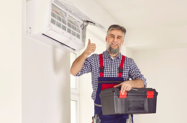 a man is holding a toolbox and giving a thumbs up in front of an air conditioner .