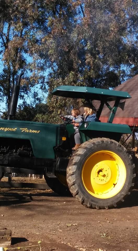 A green tractor with yellow wheels is parked in a dirt lot.