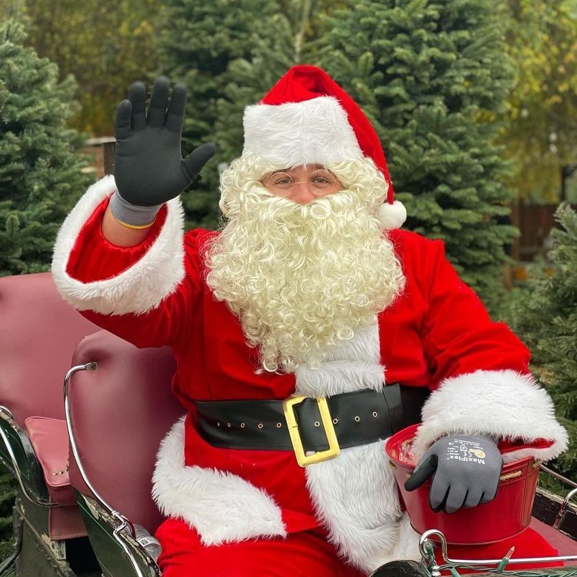 Santa Claus is sitting in a sleigh and waving.