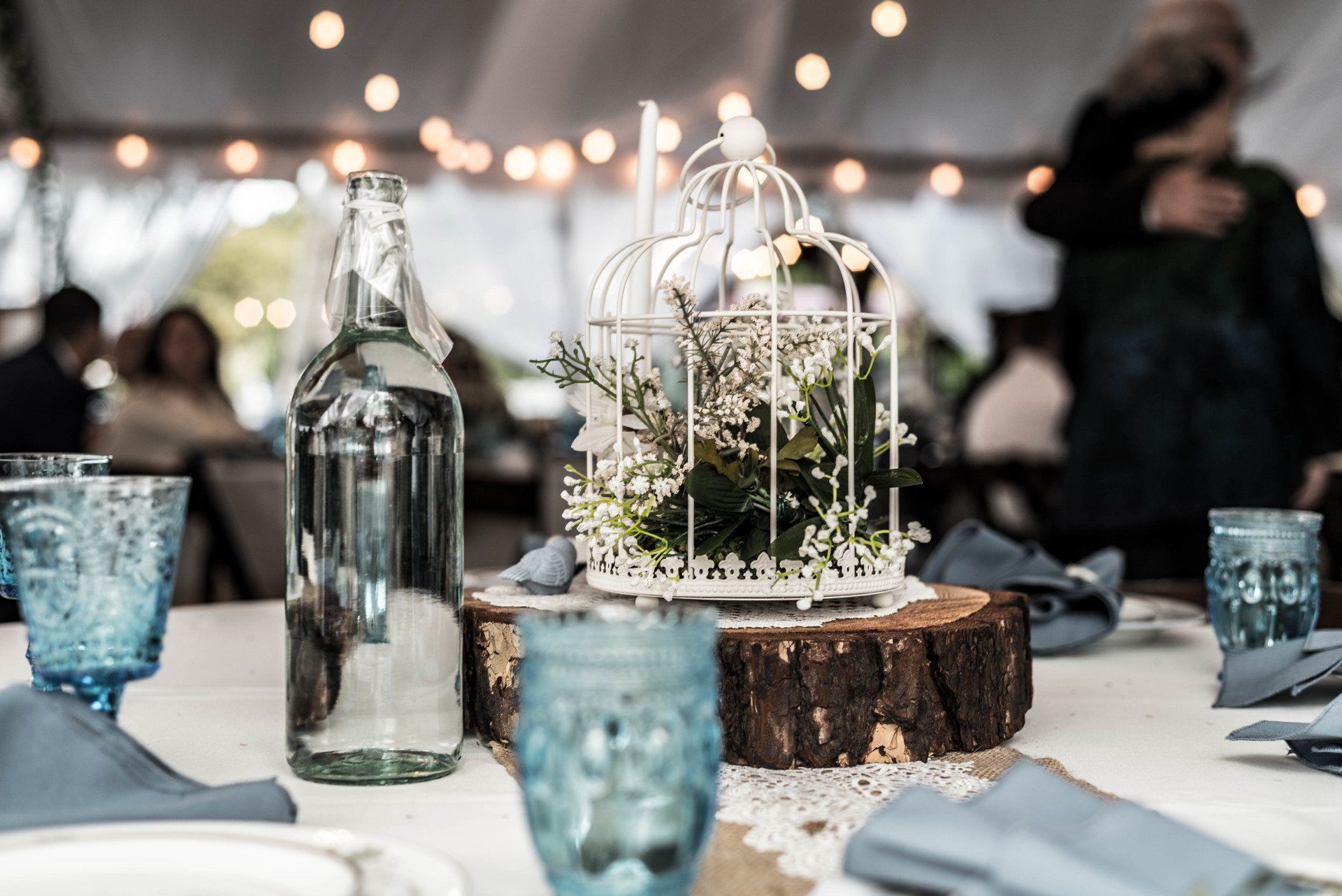 A table with a bottle of water , glasses , and a bird cage on it.