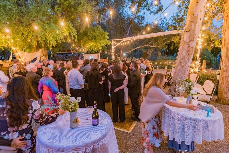 A large group of people are standing around tables at a wedding party.