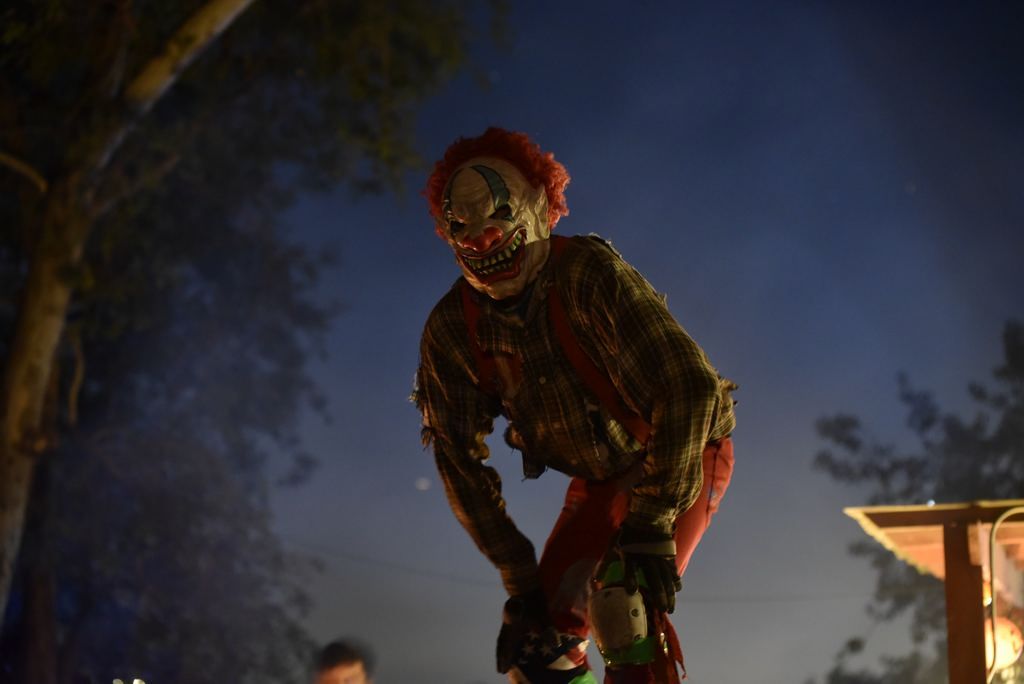 A scary clown is standing on stilts in the dark.