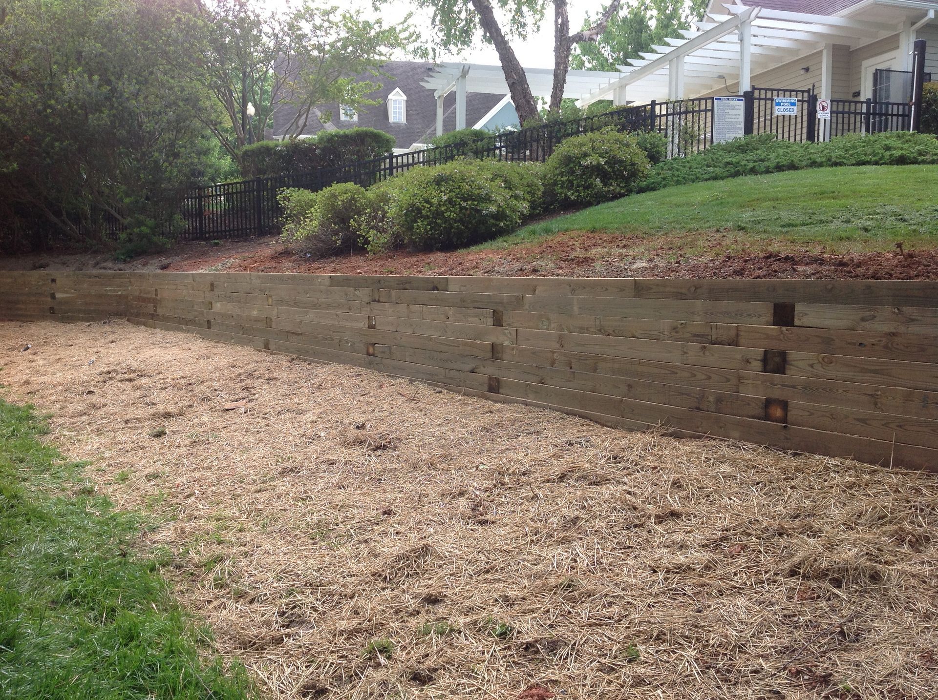 A wooden retaining wall holds back a sloped lawn. Wood chips cover the ground in front.