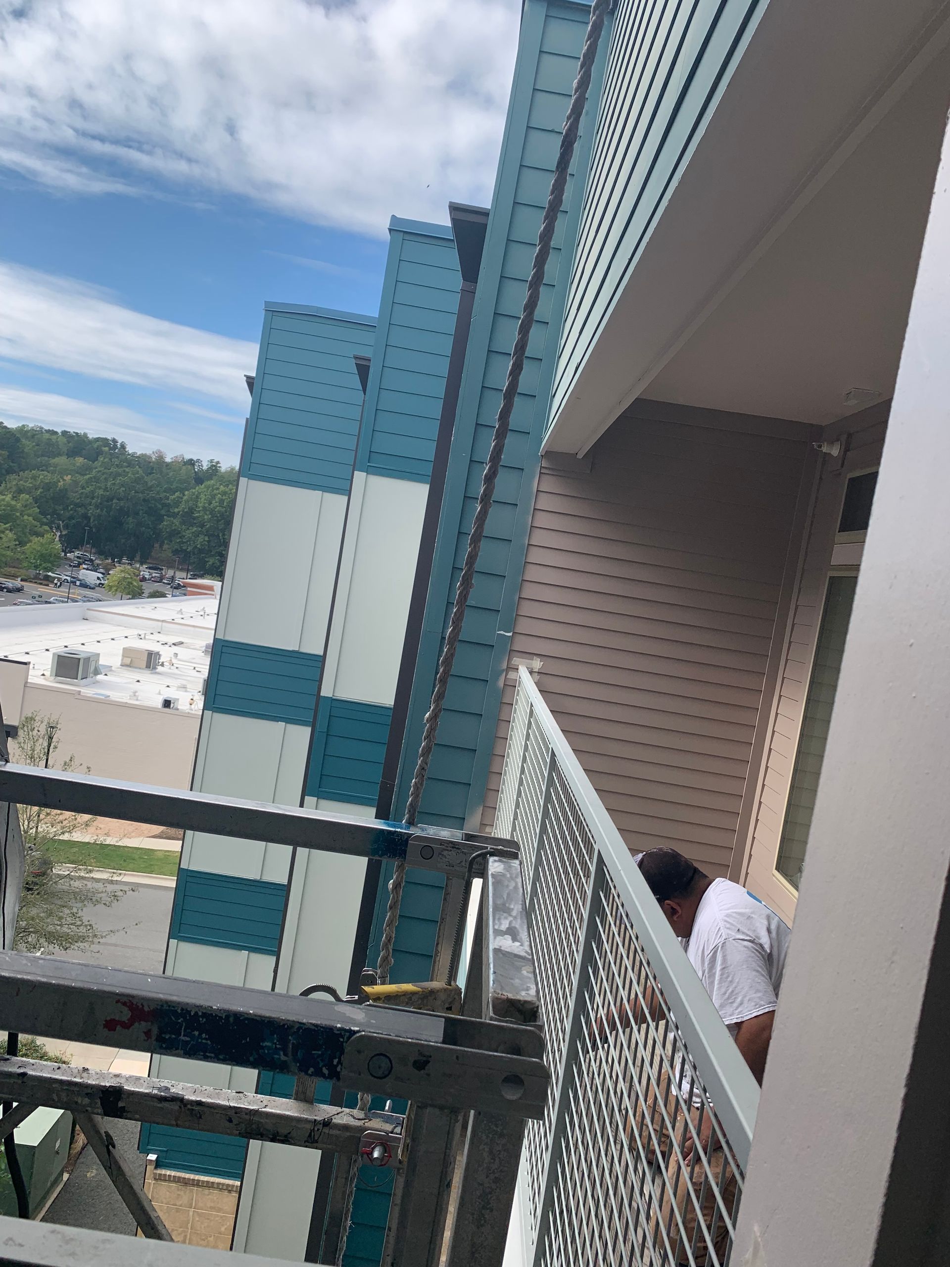 Building exterior with blue and white panels and a worker on a balcony, sunny sky.