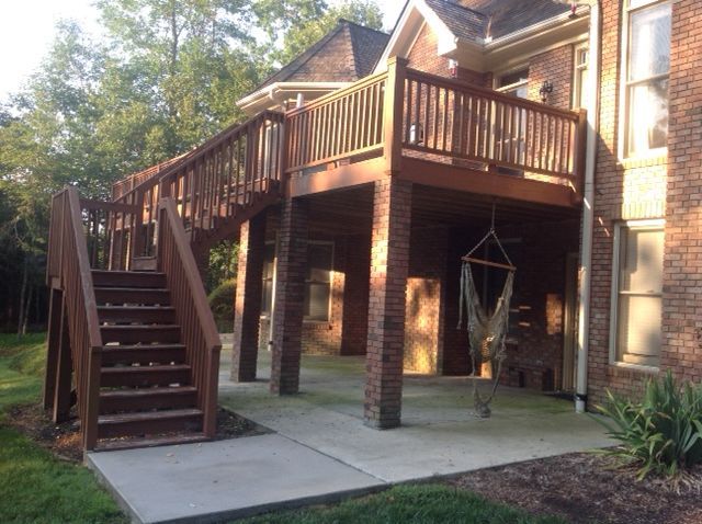 A two-story deck attached to a brick house with stairs, brown railings, and a concrete patio below.