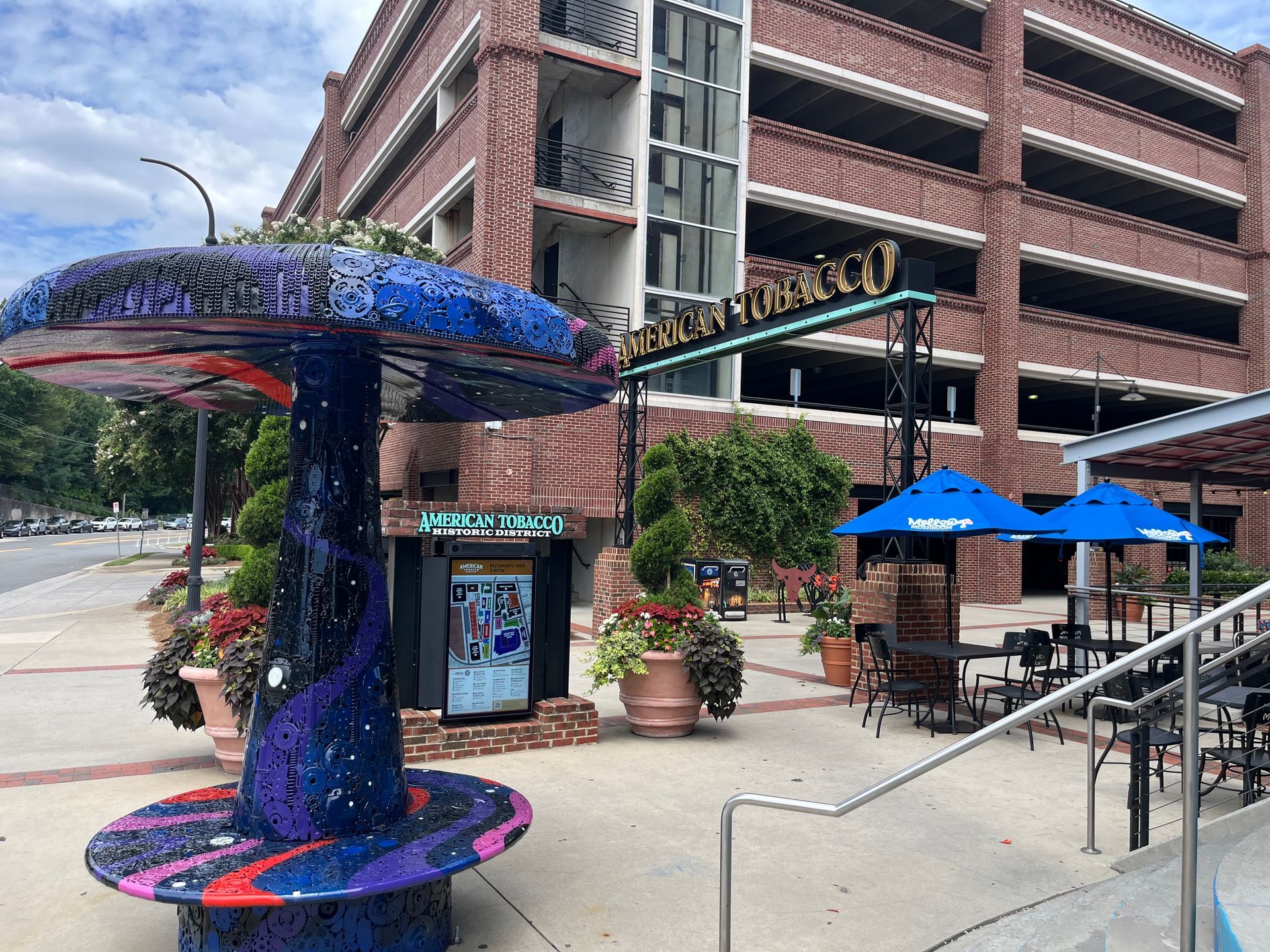 Mosaic mushroom sculpture, outdoor seating, and parking garage.