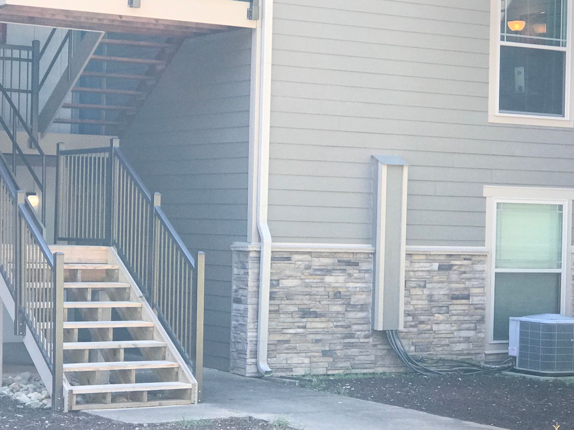 Exterior of a two-story apartment building with stairs and a stone accent on the facade.
