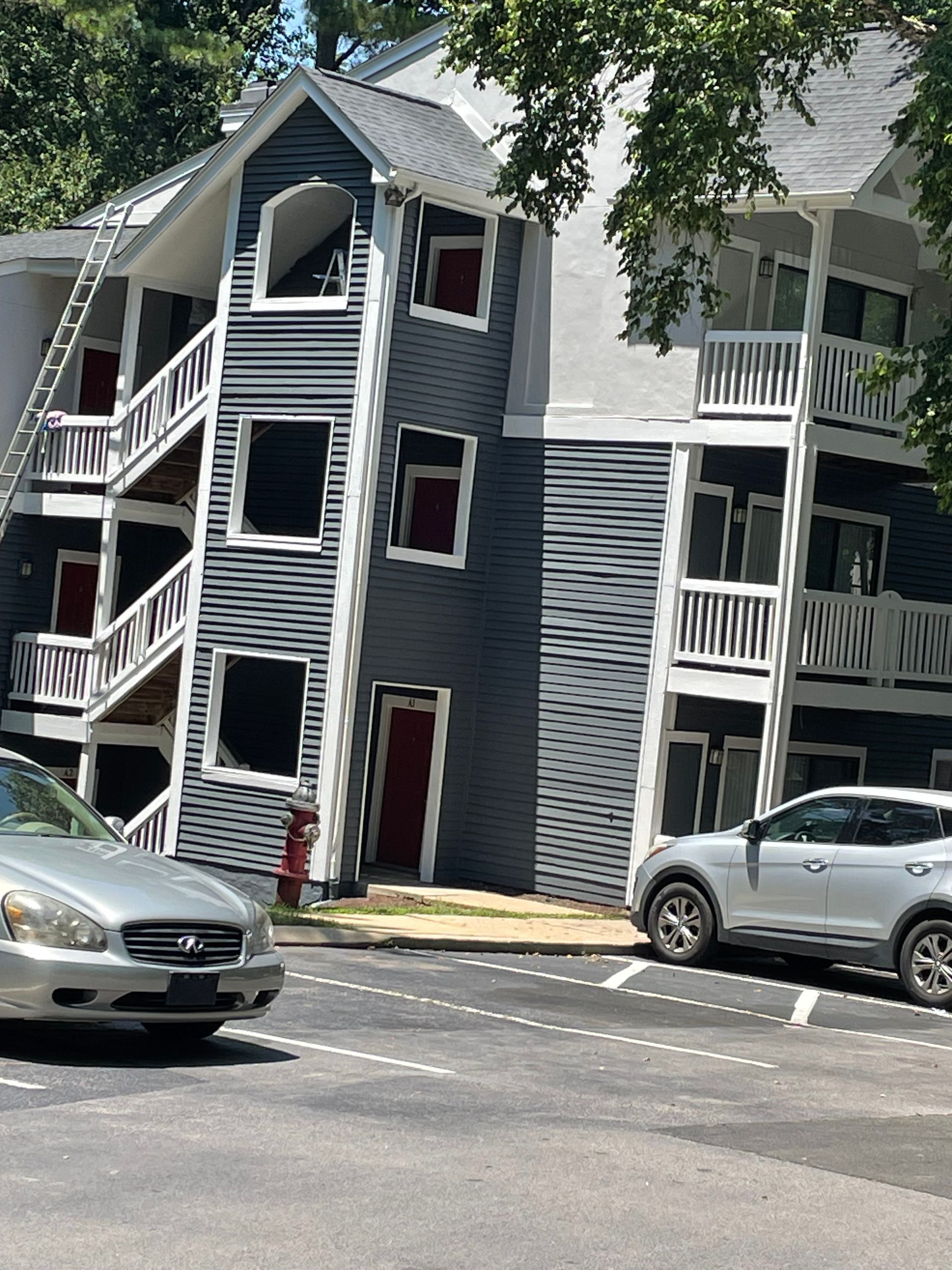 Apartment building with gray and white siding, exterior stairwells, parked cars in front.