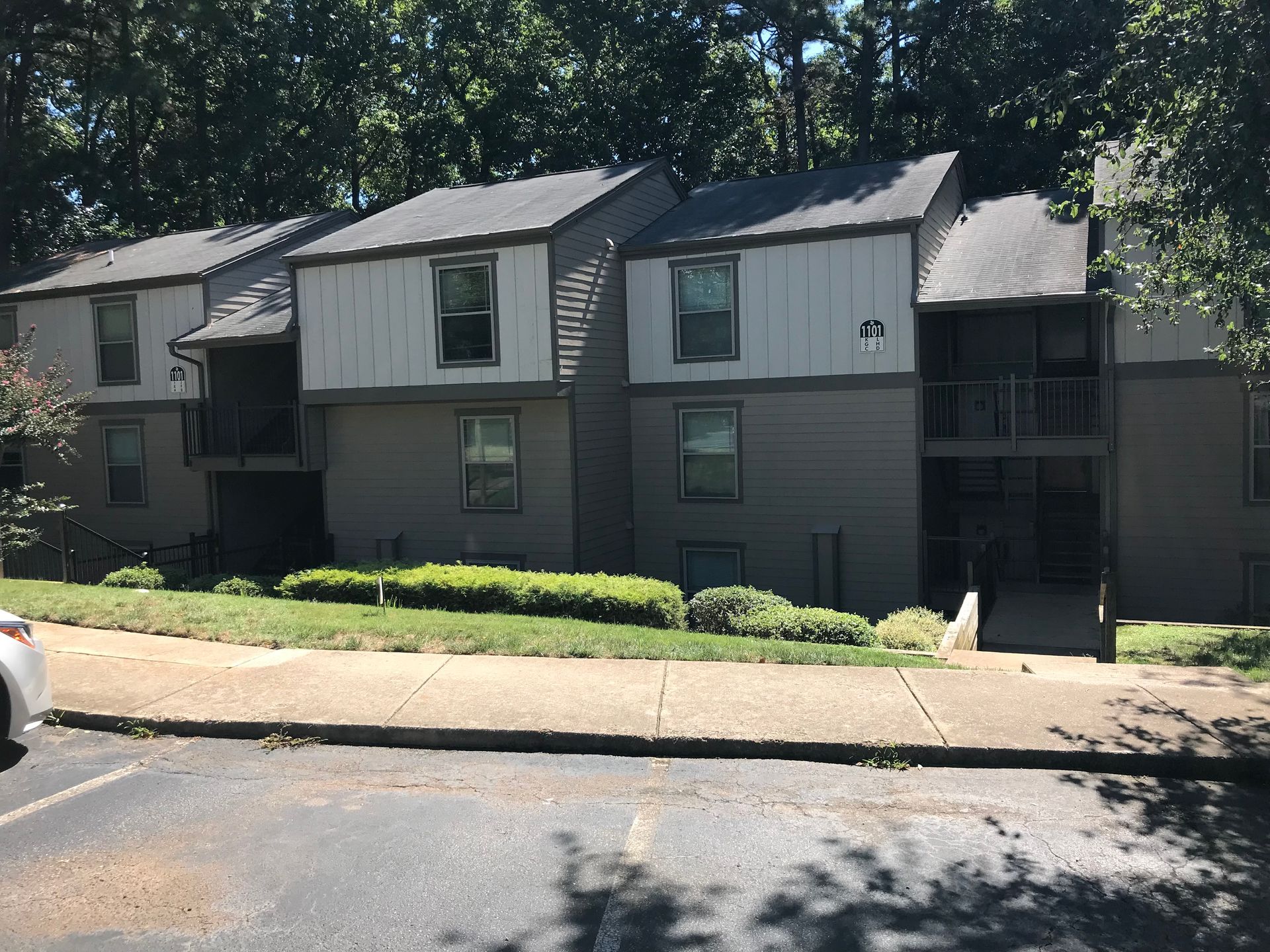 Gray and white apartment building with two stories, surrounded by trees.