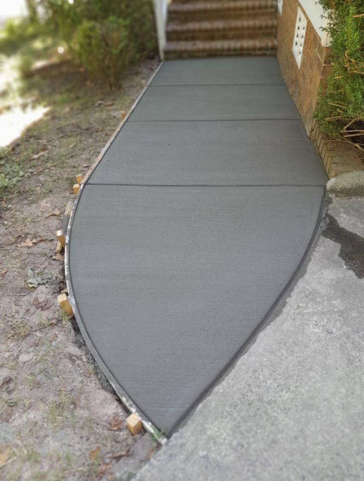 Newly poured, gray concrete walkway leading to steps of a brick building.