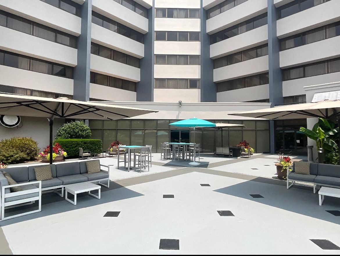 Courtyard with outdoor seating and umbrellas surrounded by a multi-story building.