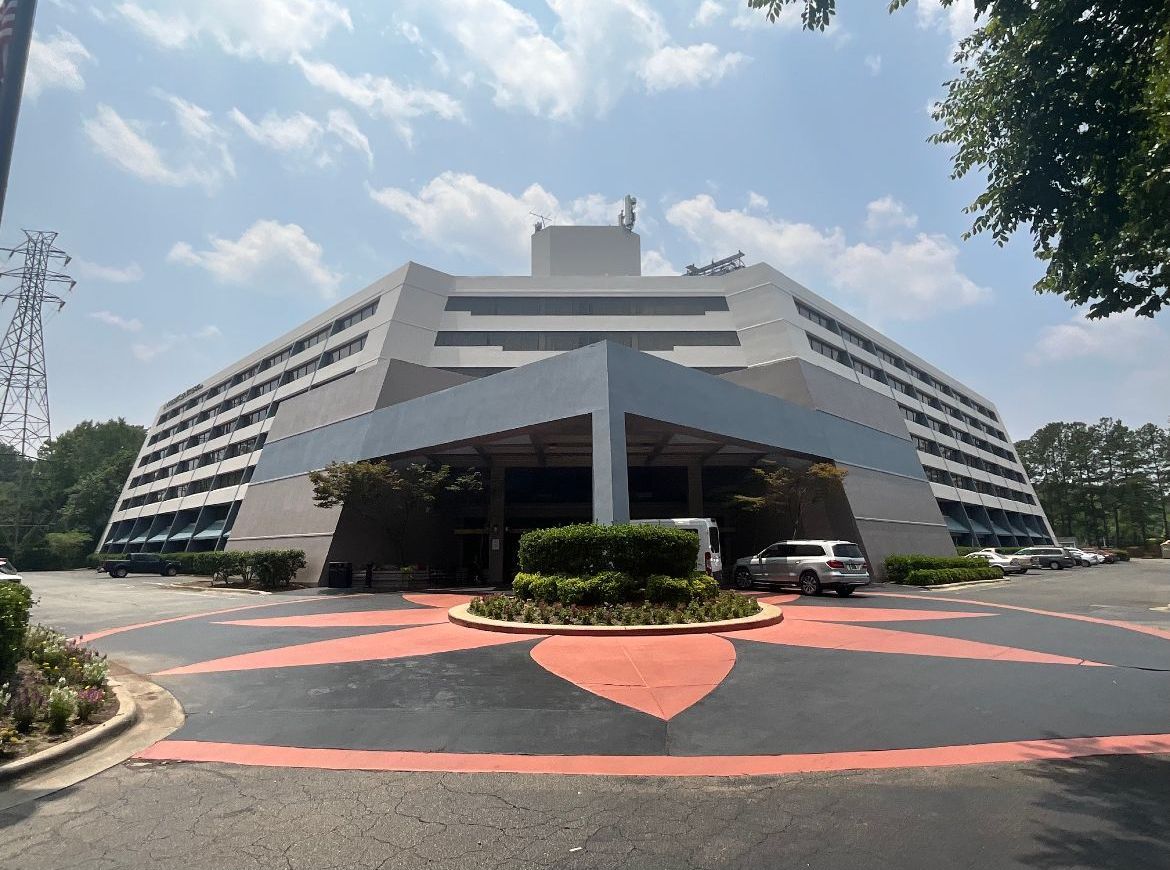 Pyramid-shaped gray hotel with a red and black circular driveway. Cars parked in front.