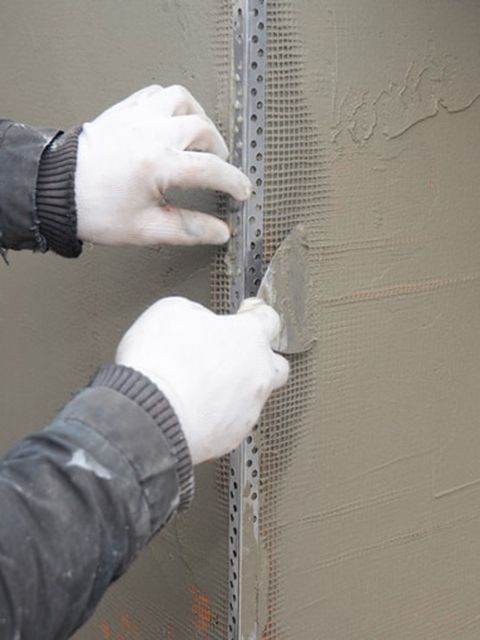 Person in gloves using a trowel to apply stucco around a metal corner bead on a wall.