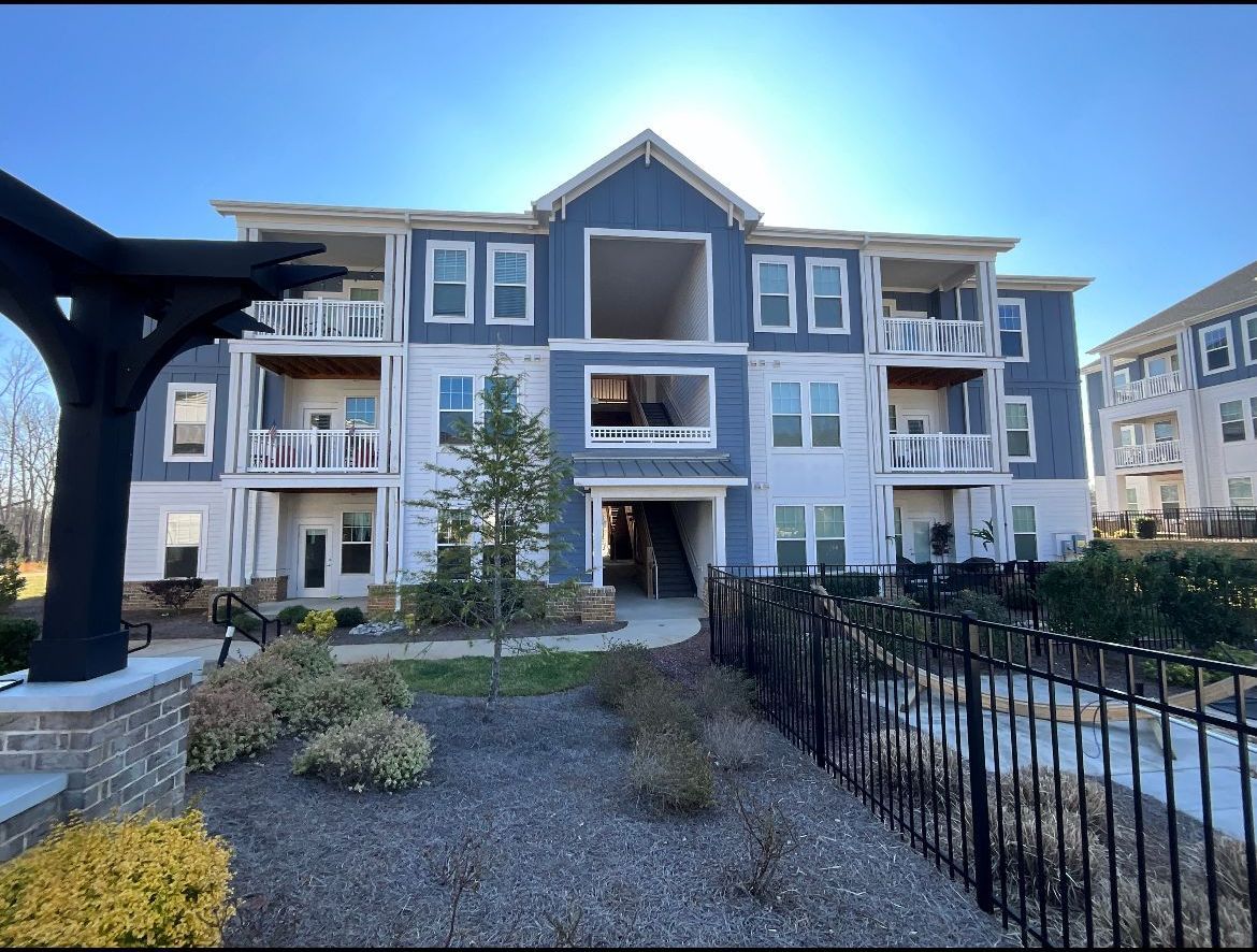 Multi-story apartment building under construction, blue and white siding, wrought iron fence, sunny day.