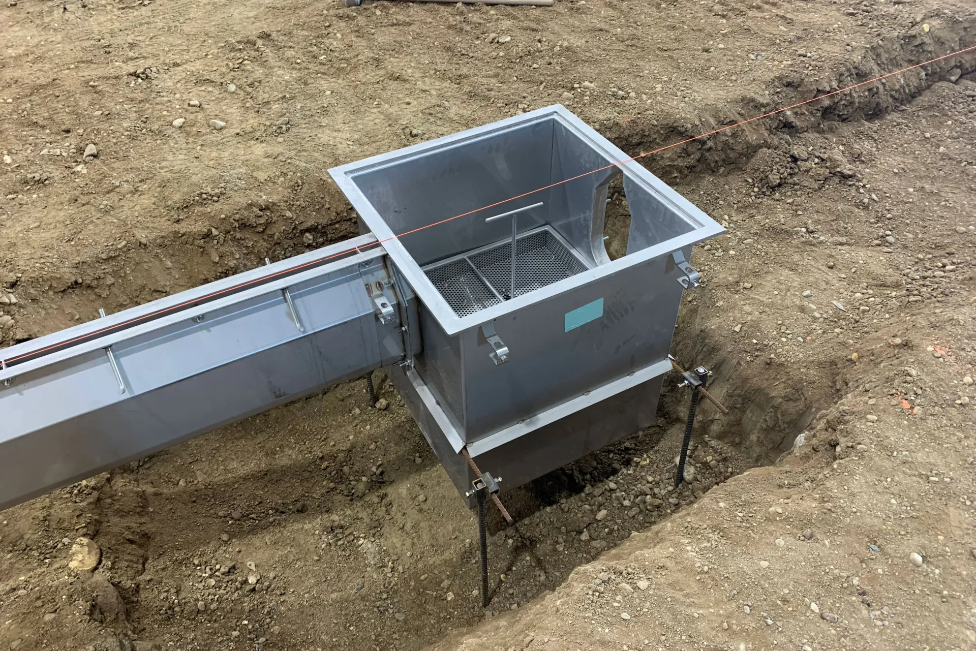 Metal drainage system installation in a dirt trench, with grate and connected channel.