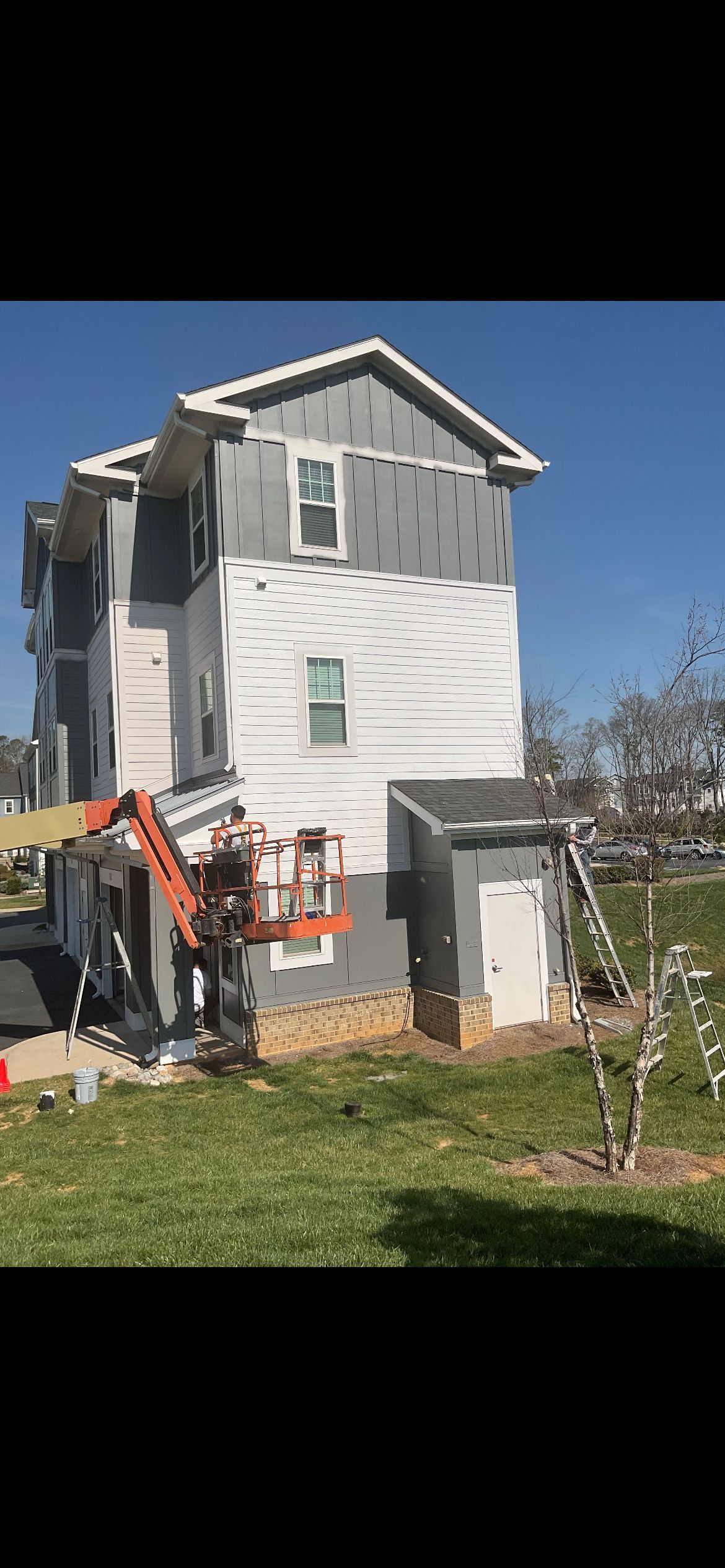Building with siding being installed, an orange lift, and blue sky.