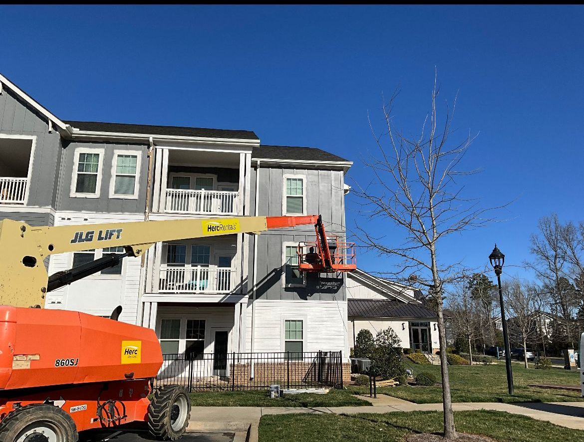 Construction workers in an orange lift are working on a grey apartment building on a sunny day.