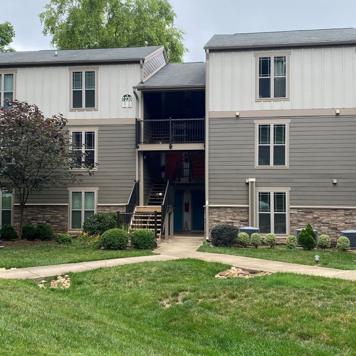 Apartment building with two floors and central staircase; gray siding, tan trim, and green lawn.