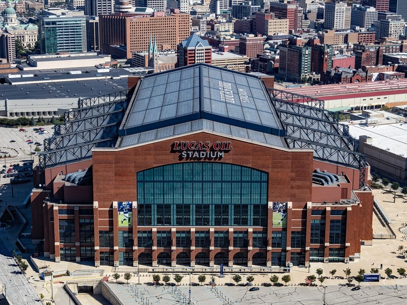 Lucas Oil Stadium in Indianapolis, brick exterior, glass roof, surrounded by buildings and parking lots.