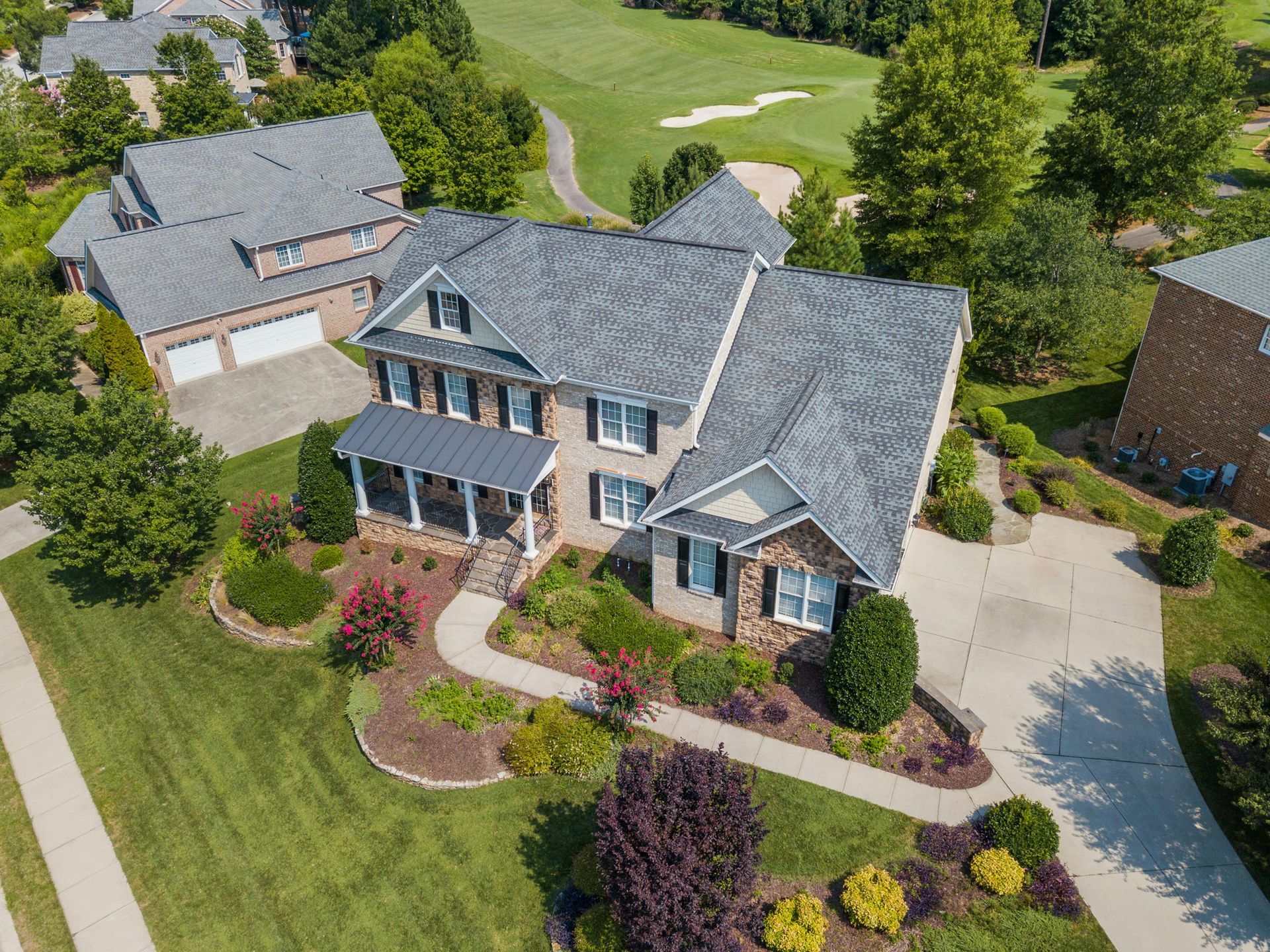 White house with light blue gable siding and brown roof on a sunny day. Green lawn and trees.