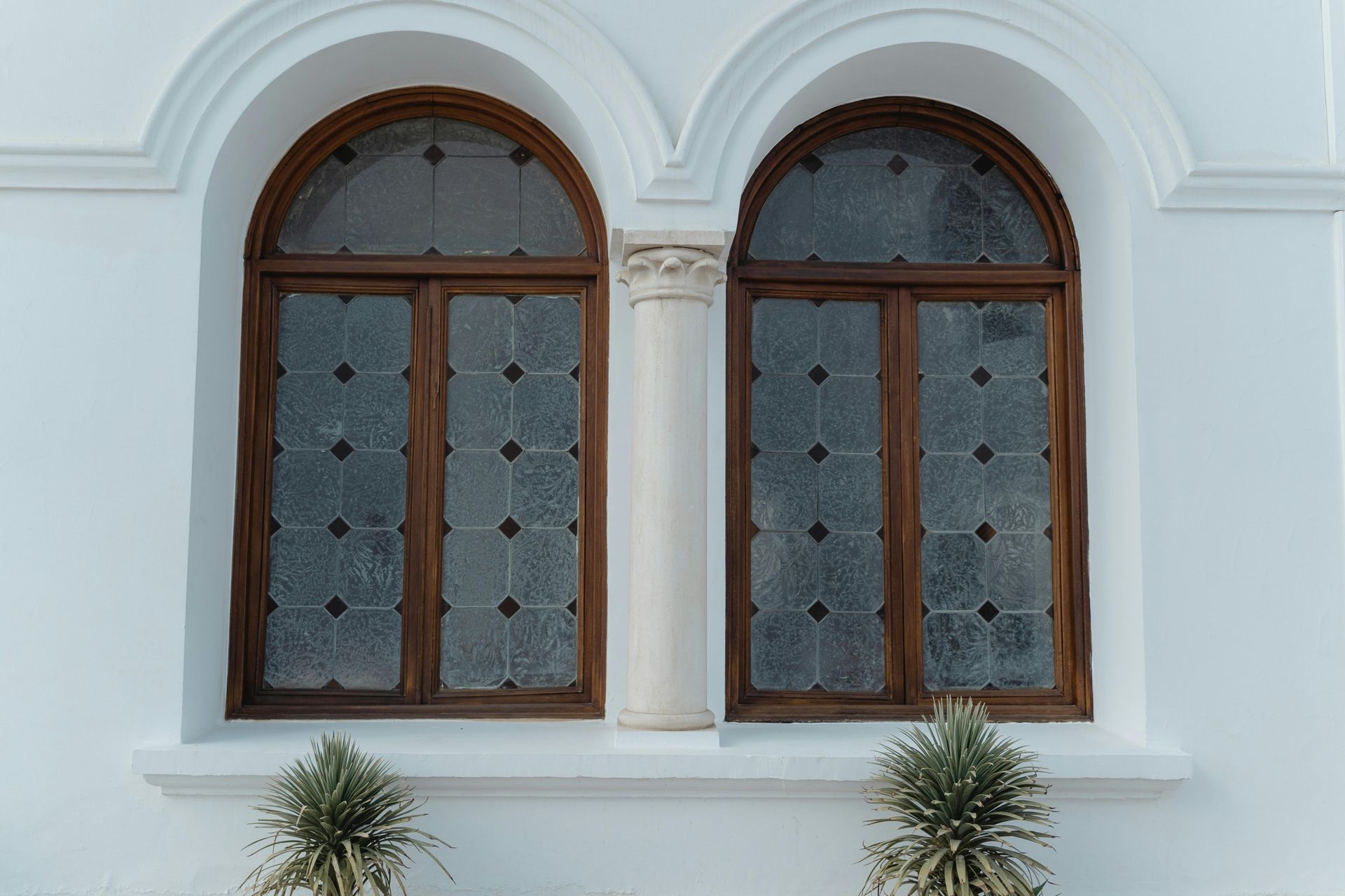 Two arched wooden windows with decorative glass panes set in a white building.