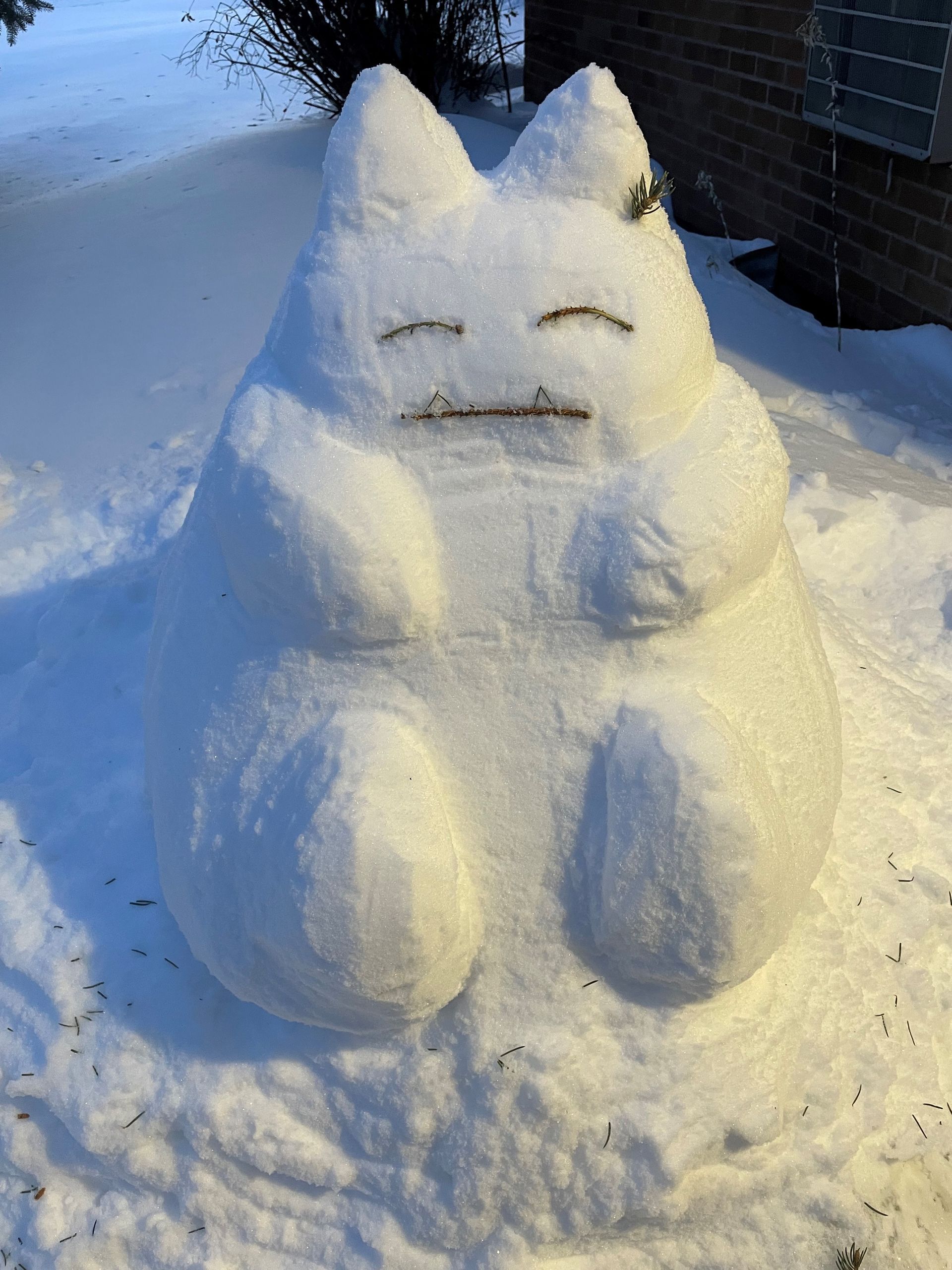 A snow sculpture of snorlax from pokemon is sitting in the snow.