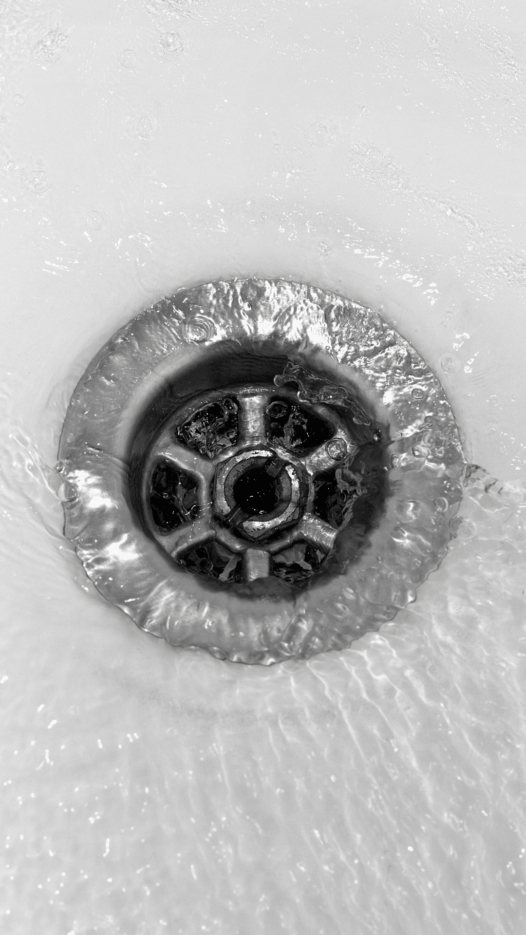 A black and white photo of water running down a sink drain.