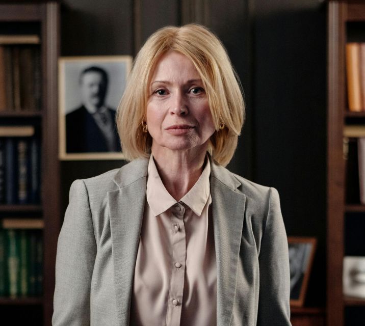 Een vrouw in een pak staat voor een boekenplank