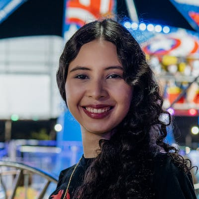 Een vrouw met lang krullend haar staat lachend voor een reuzenrad.