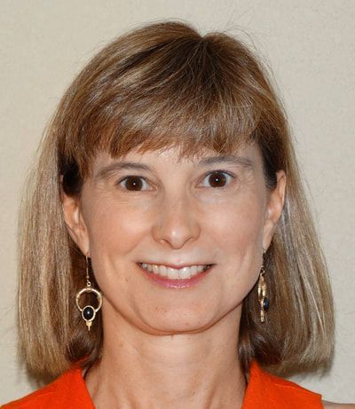 A woman wearing earrings and an orange shirt smiles for the camera