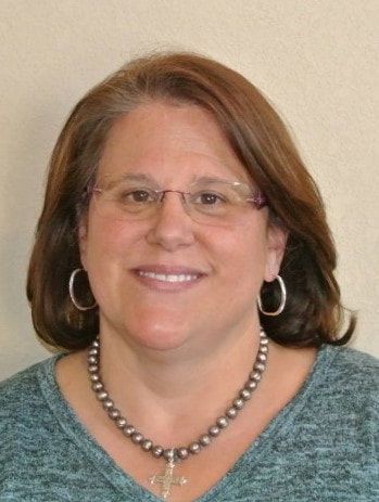 A woman wearing glasses and a necklace is smiling for the camera.