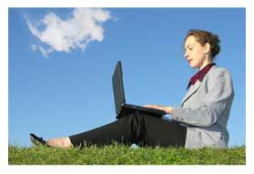 A woman is sitting on the grass using a laptop computer.