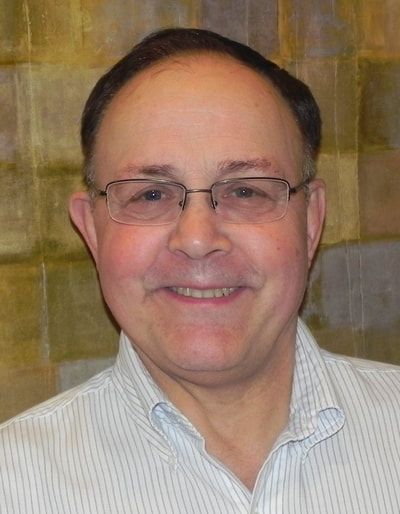 A man wearing glasses and a striped shirt is smiling for the camera.