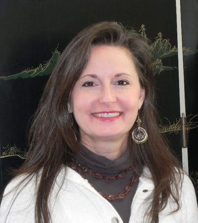 A woman wearing a white jacket and earrings is smiling for the camera.