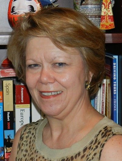 A woman in a leopard print shirt is smiling in front of a bookshelf with spanish books on it