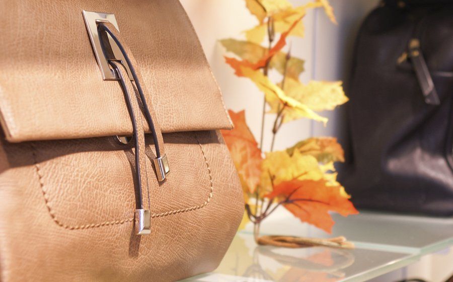 Auf einem Glastisch liegt neben einer Vase mit Blumen eine Handtasche.