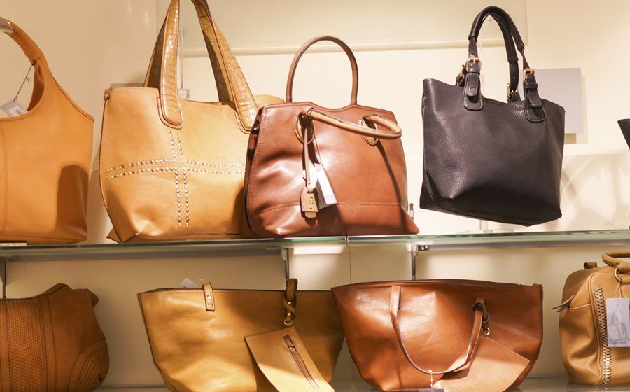 Auf einem Glasregal sind mehrere Handtaschen aus braunem Leder ausgestellt.
