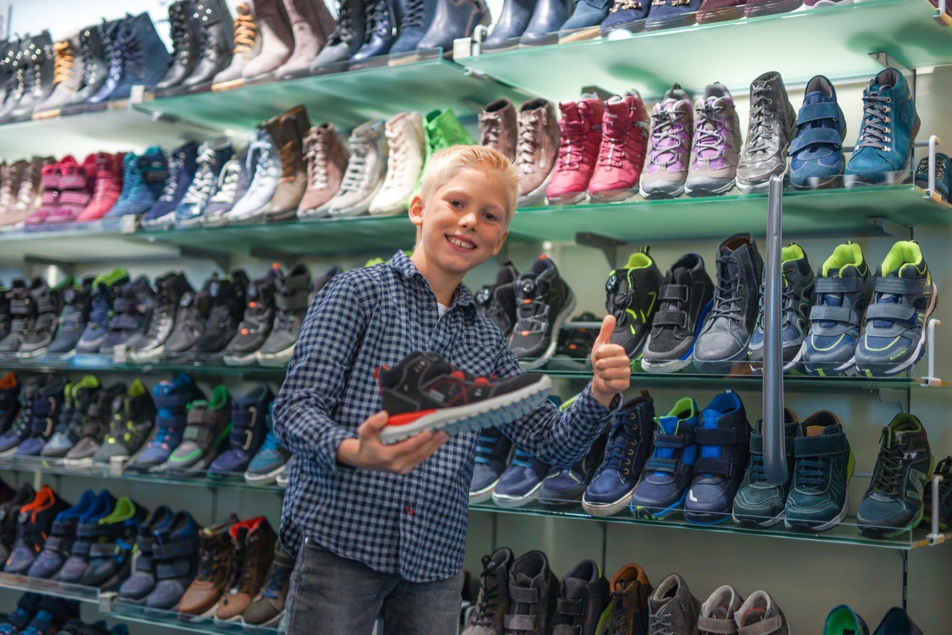 Ein kleiner Junge hält in einem Schuhgeschäft ein Paar Schuhe in der Hand.
