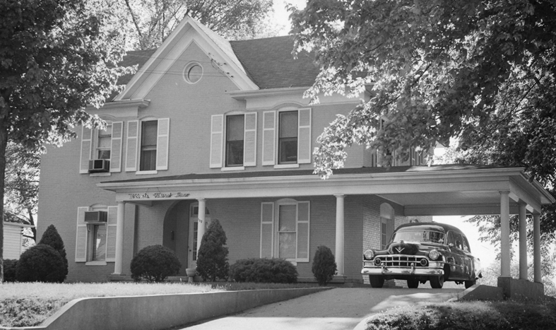 A black and white photo of a house with a car parked underneath it