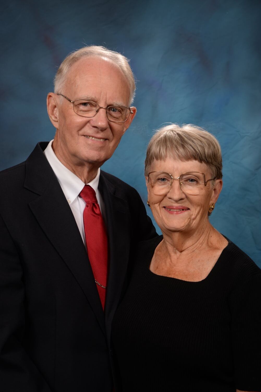A man and woman are posing for a picture in front of a blue background.