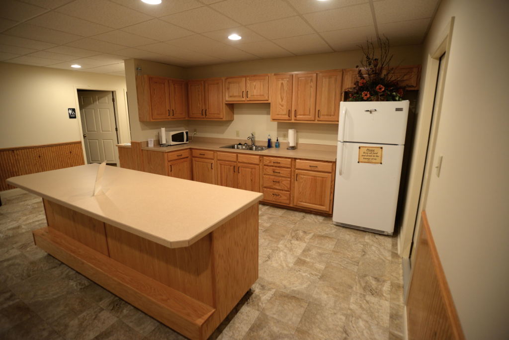 A kitchen with wooden cabinets , a large island , a refrigerator and a sink.
