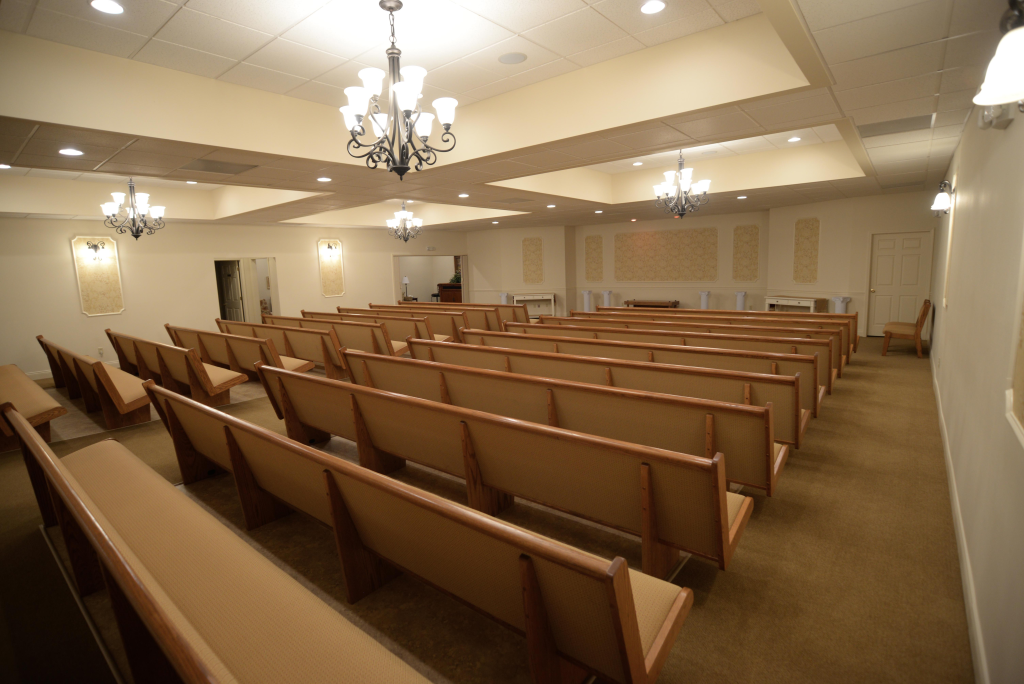 A church with rows of wooden benches and a chandelier hanging from the ceiling.
