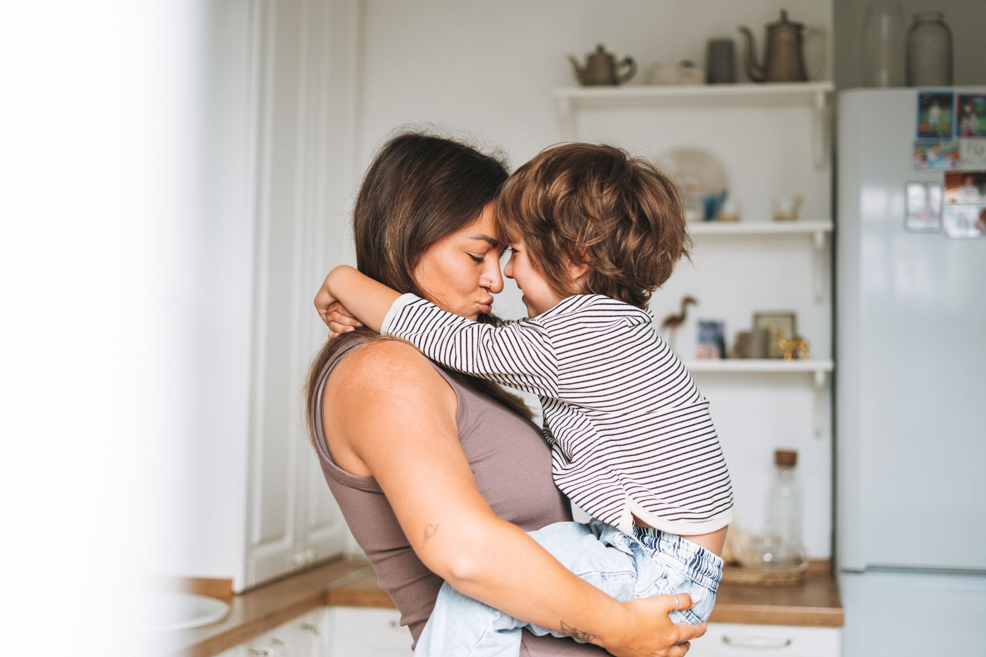 A woman is holding a little boy in her arms in a kitchen.