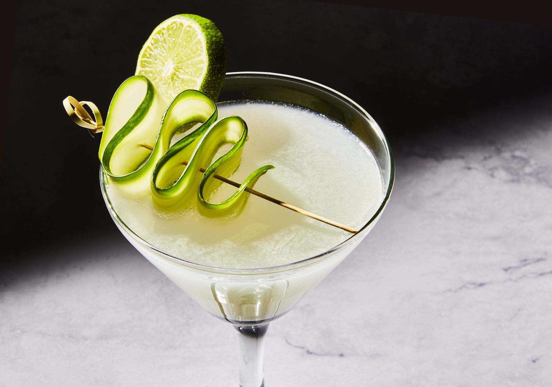 A martini with cucumber slices on a stick in it